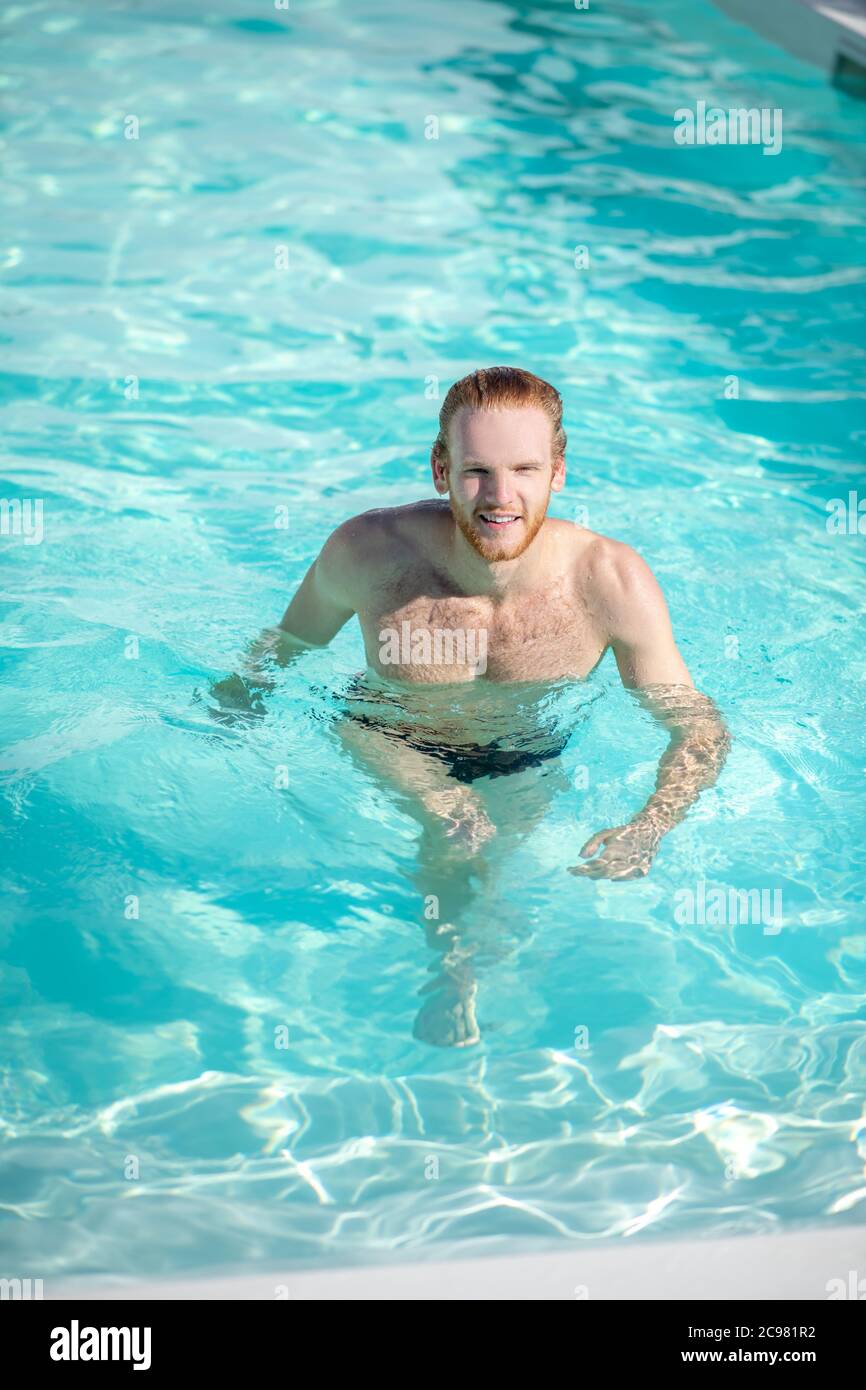 Giovane uomo felice che cammina in acqua in piscina Foto Stock