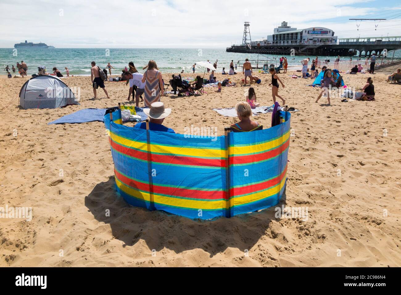 Break vento / break eretto da una famiglia turistica in una giornata ventosa sulla spiaggia di Bournemouth in Dorset. UK (120) Foto Stock