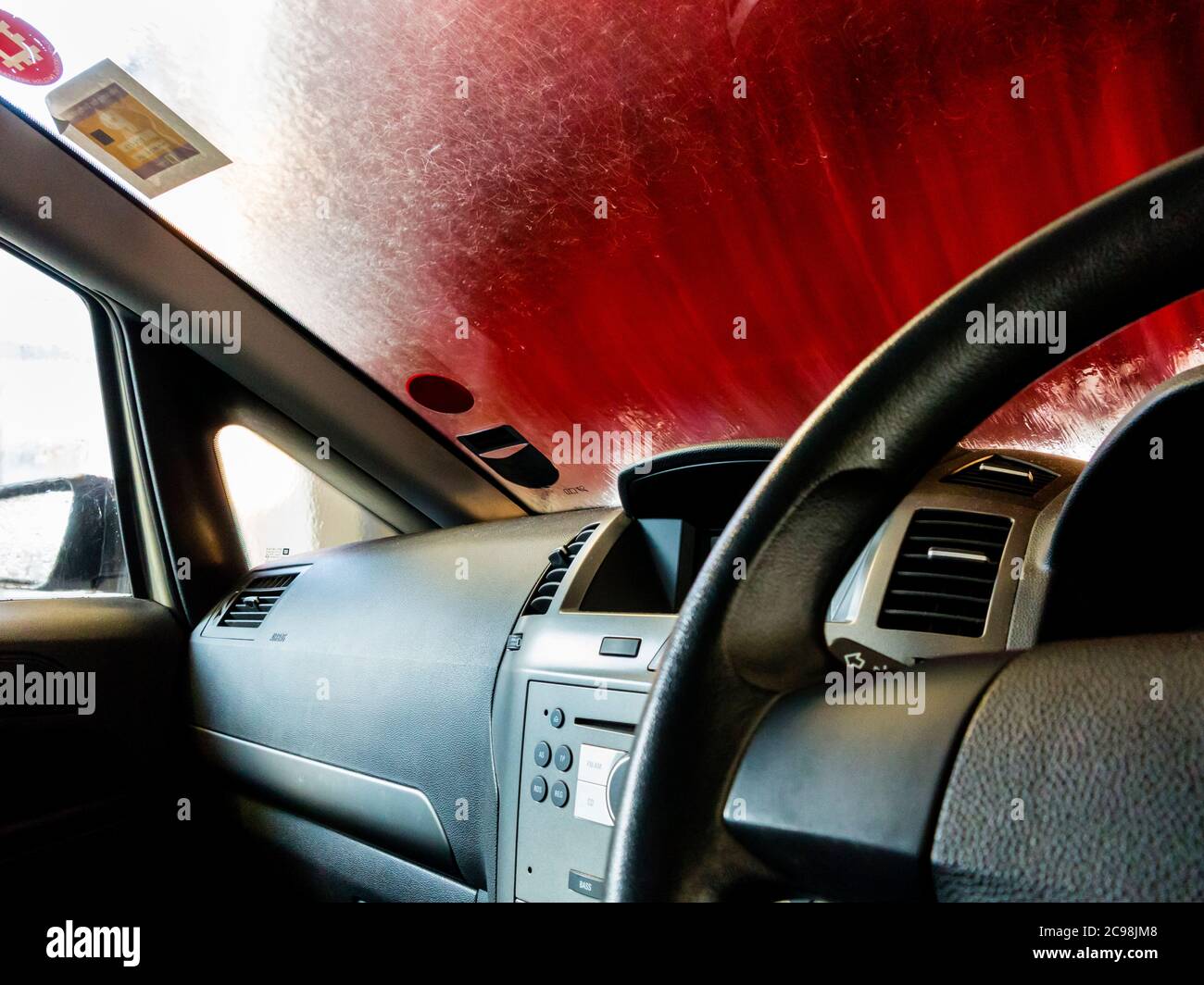 Vista attraverso il parabrezza di un'auto mentre passa attraverso un autolavaggio automatico con il volante in primo piano. Foto Stock