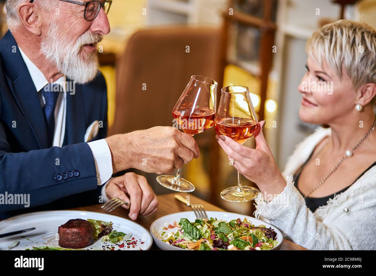 Bella coppia anziana hanno un pasto in un ristorante personale, innamorati. Drink maschile e femminile con capelli grigi e bicchieri di vongolatura con champagne. Foto Stock