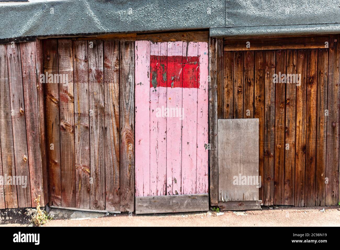 Decrepit porta garage in legno con profilo porta di accesso rosa dipinto a Southend on Sea, Essex, UK. Area urbana. Struttura in decadimento Foto Stock