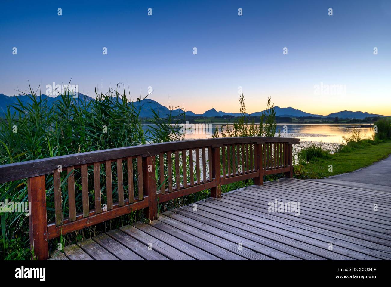 Ponte di legno sul lungomare del lago Hopfensee, con le Alpi Allgäu sullo sfondo, Allgäu, Schwaben, Baviera, Germania Foto Stock