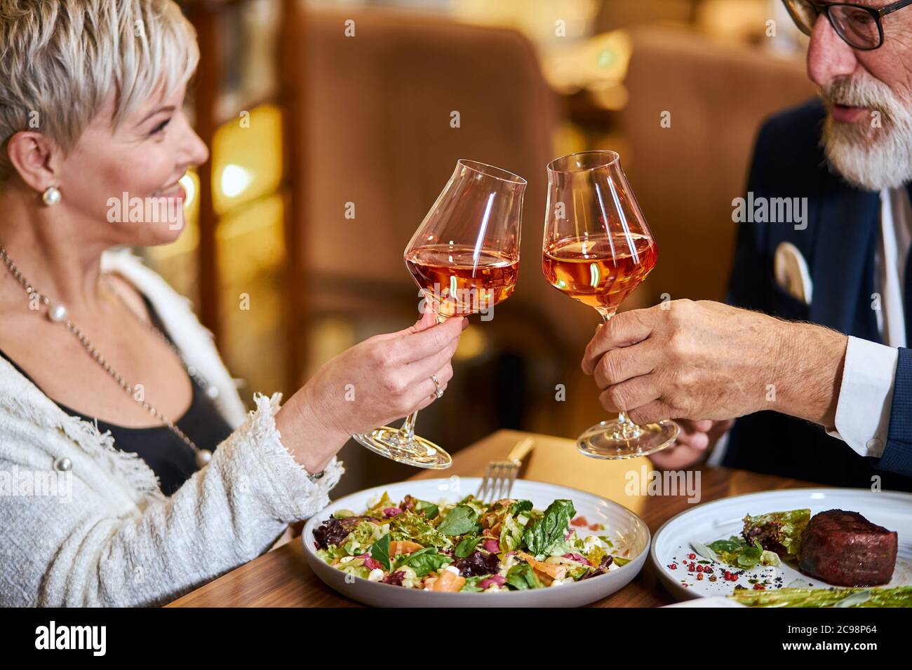 Bella coppia anziana hanno un pasto in un ristorante personale, innamorati. Drink maschile e femminile con capelli grigi e bicchieri di vongolatura con champagne. Foto Stock