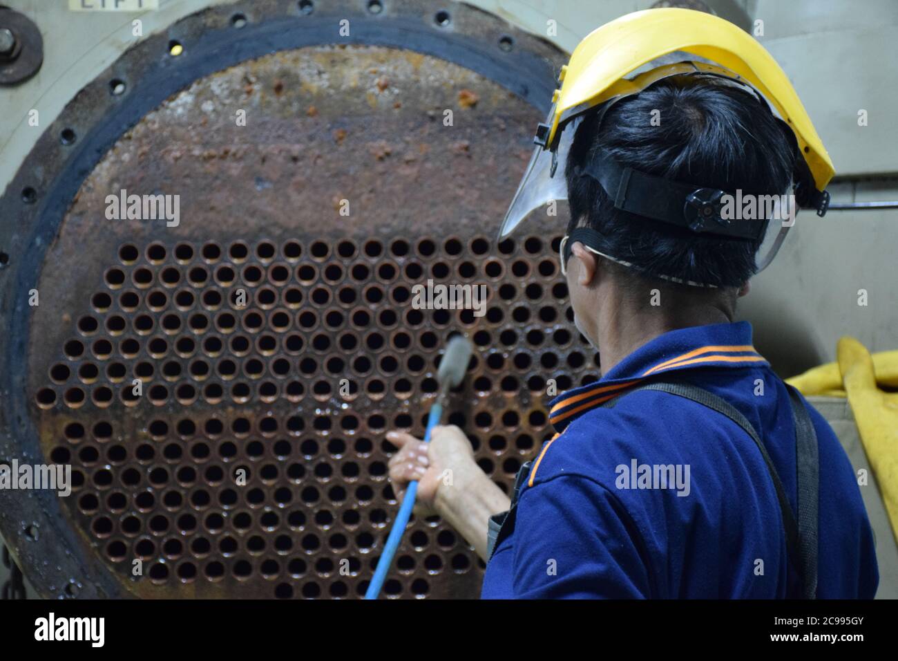 Il meccanico utilizza la spazzola per pulire il tubo del condensatore del refrigeratore - impianto HVAC. Foto Stock