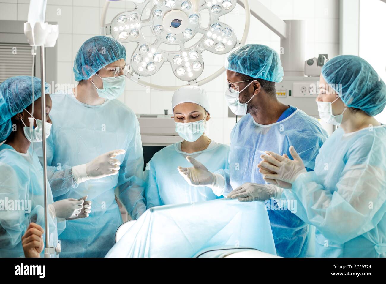 uomo caucasico e uomo afro in maschere che hanno un ergumento durante il trattamento del paziente in sala operatoria Foto Stock