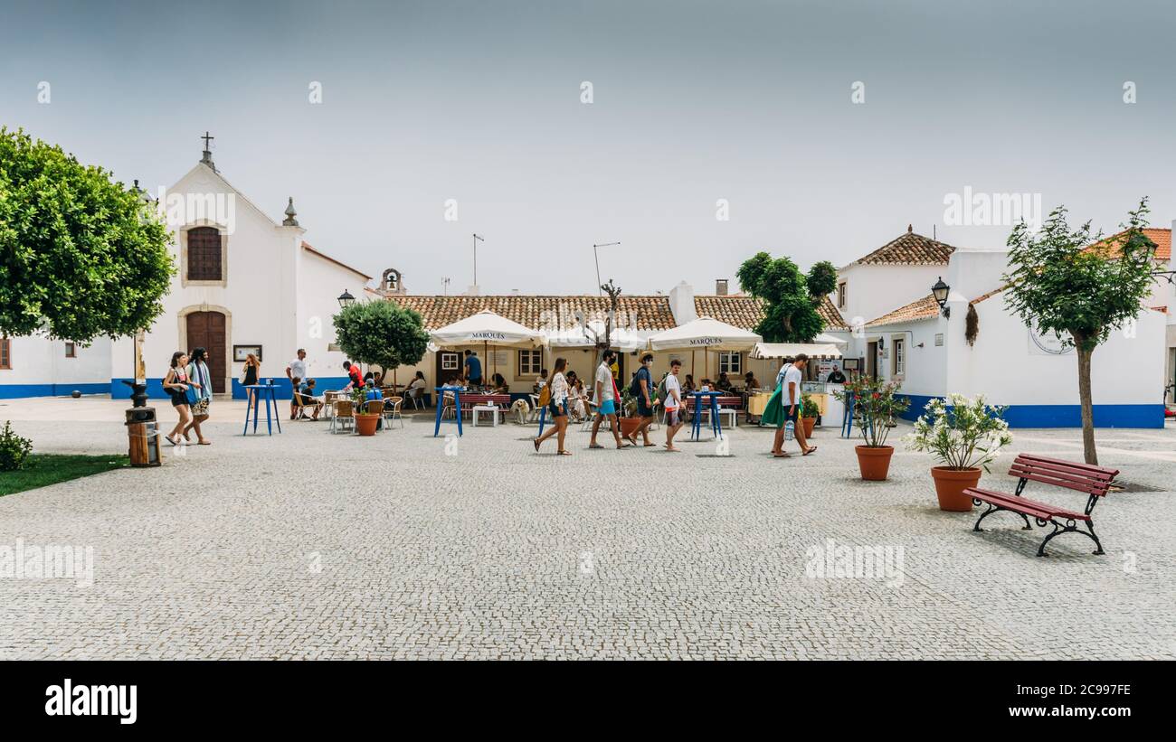 La piazza principale con la gente che si rilassa ai caffè a Picturreche Porto Covo in Portogallo Foto Stock