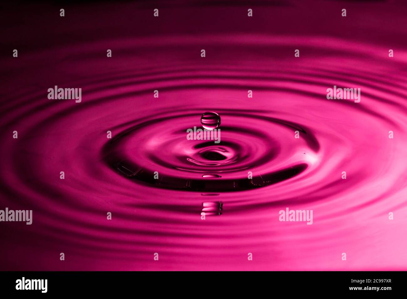 Gocce d'acqua perfette che spruzzano in acqua liscia causando increspature un colore rosa Foto Stock