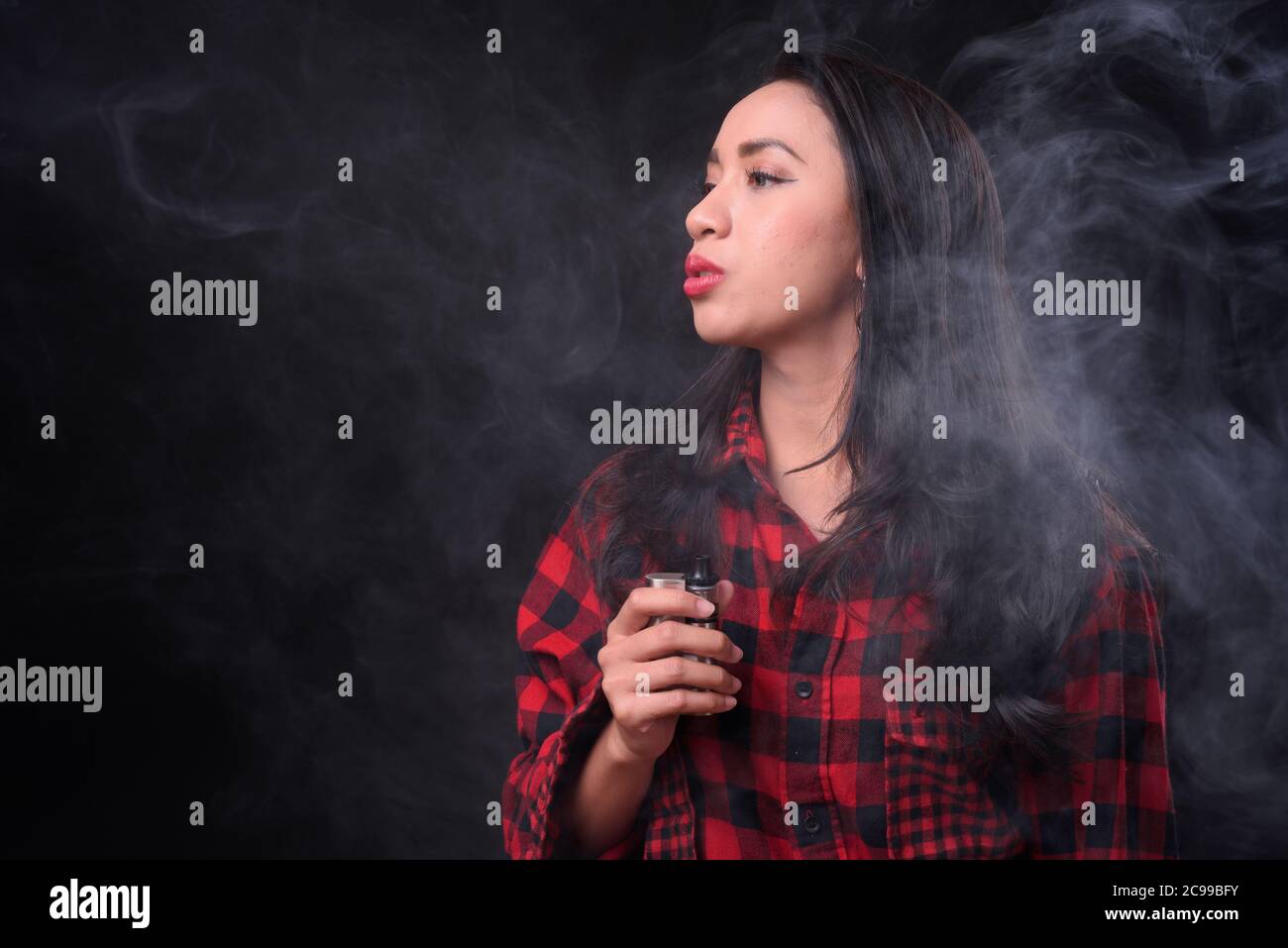 Giovane bella donna asiatica che vaping su sfondo nero Foto Stock
