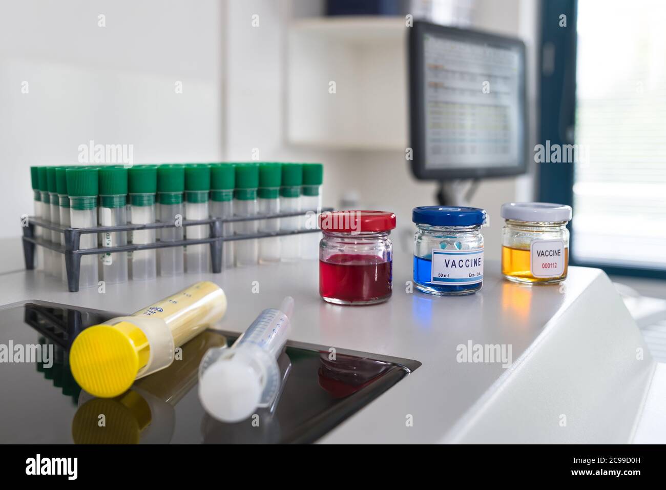 Ricerca sul vaccino del coronavirus in laboratorio scientifico con software medico sullo schermo del computer. Flaconcini di vetro con liquido rosso, blu o giallo o siringhe. Foto Stock