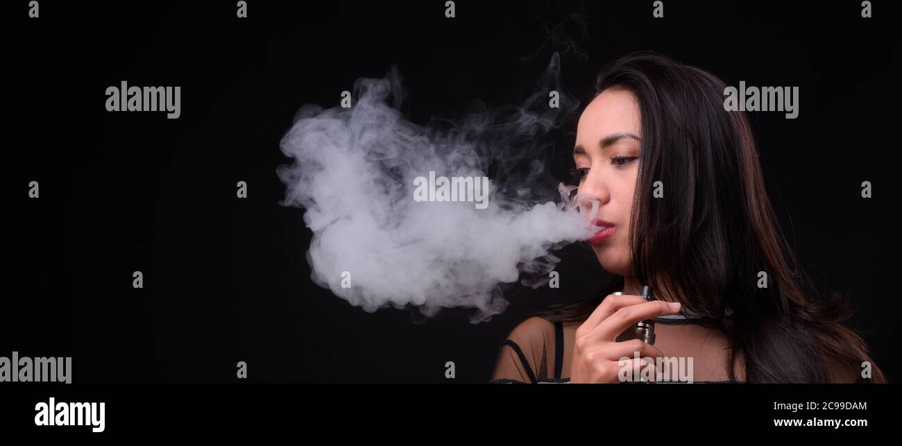 Giovane bella donna asiatica che vaping su sfondo nero Foto Stock