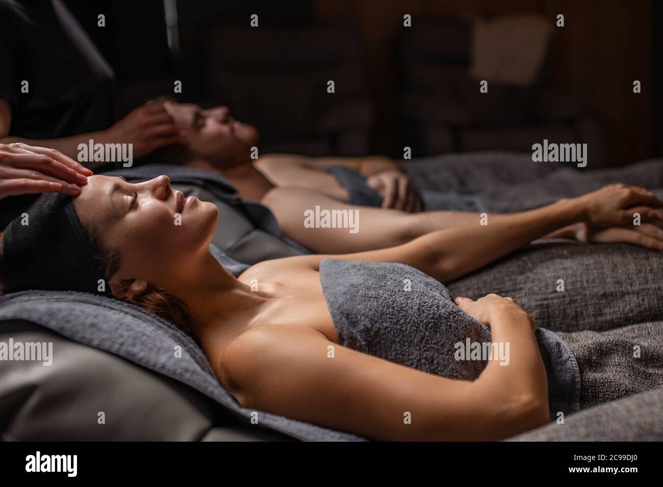 felice coppia sposata che si trova sulle scrivanie di massaggio nel salone di bellezza, l'uomo e la donna ottengono la procedura cosmetic di bellezza, prenda la cura della pelle sulla testa e sul viso, ligt del viso a. Foto Stock