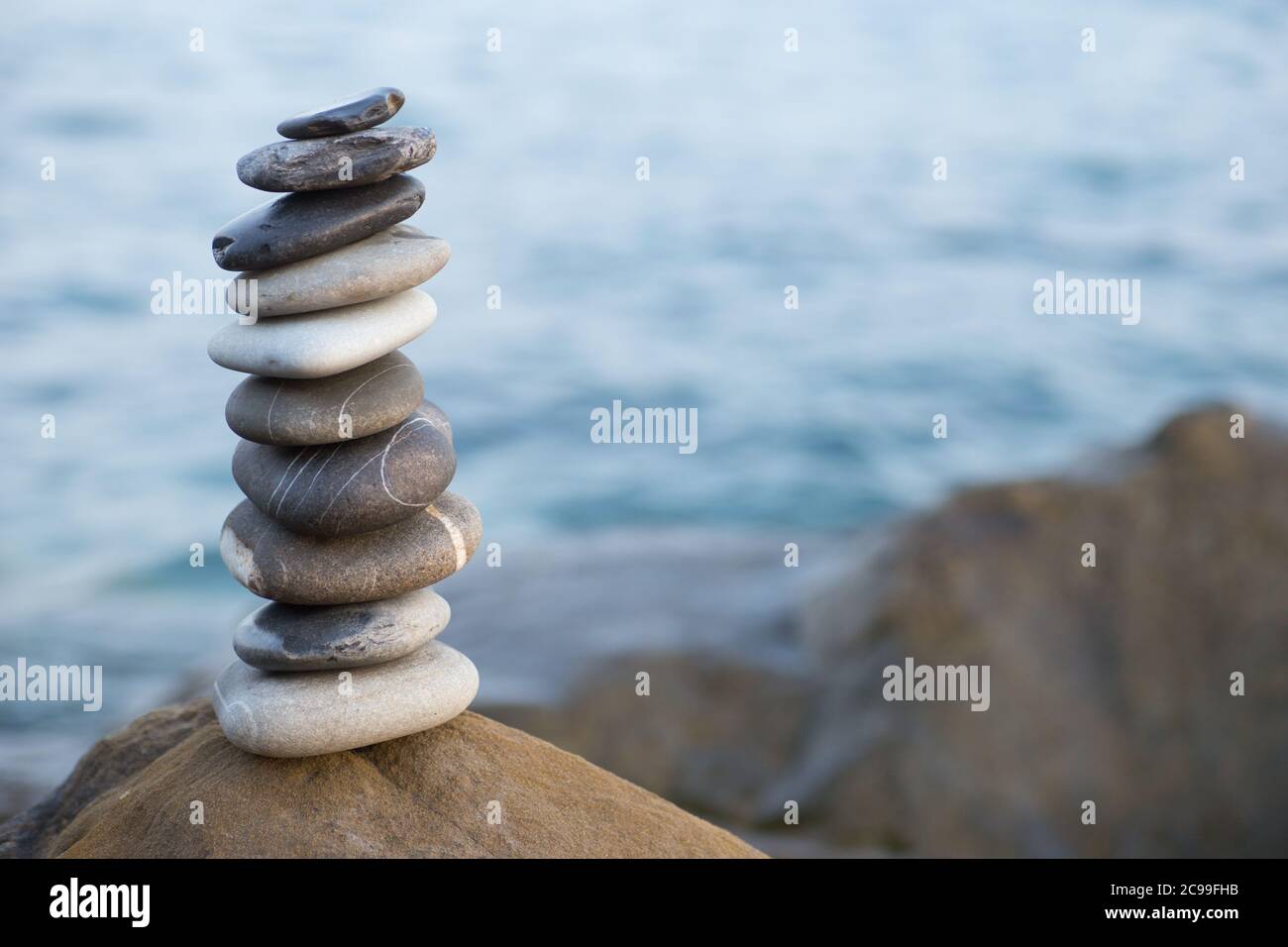 Pietre piramide sulla sabbia simboleggiando zen, armonia, equilibrio. Oceano al tramonto sullo sfondo. Foto Stock