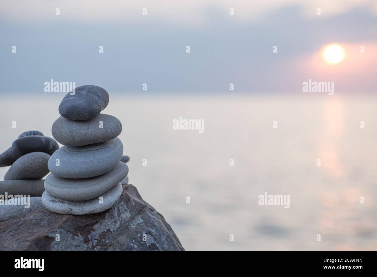 Pietre piramide sulla sabbia simboleggiando zen, armonia, equilibrio. Oceano al tramonto sullo sfondo. Foto Stock