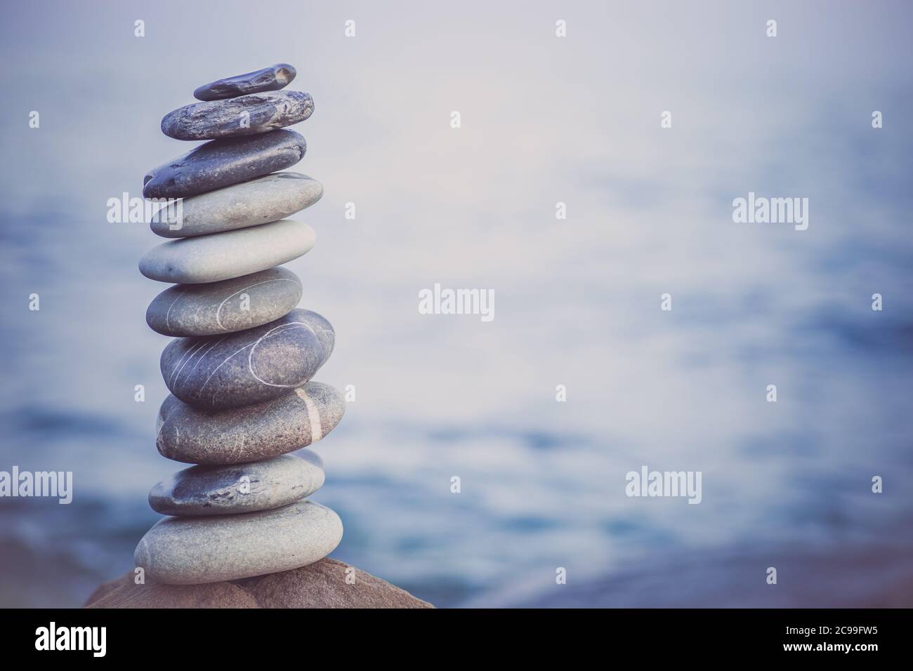 Pietre piramide sulla sabbia simboleggiando zen, armonia, equilibrio. Oceano al tramonto sullo sfondo. Foto Stock