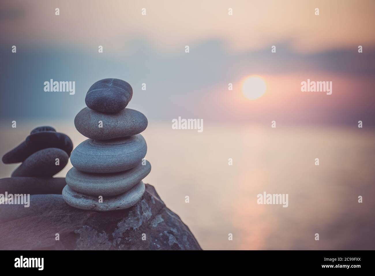 Pietre piramide sulla sabbia simboleggiando zen, armonia, equilibrio. Oceano al tramonto sullo sfondo. Foto Stock