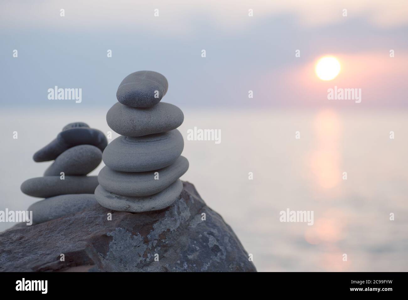Pietre piramide sulla sabbia simboleggiando zen, armonia, equilibrio. Oceano al tramonto sullo sfondo. Foto Stock