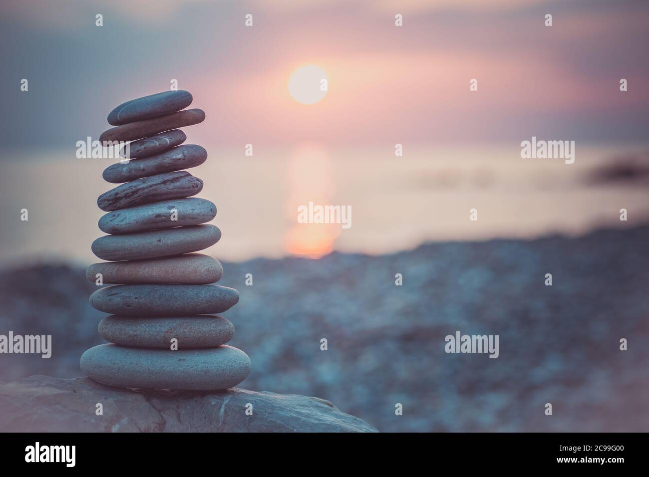 Pietre piramide sulla sabbia simboleggiando zen, armonia, equilibrio. Oceano al tramonto sullo sfondo. Foto Stock