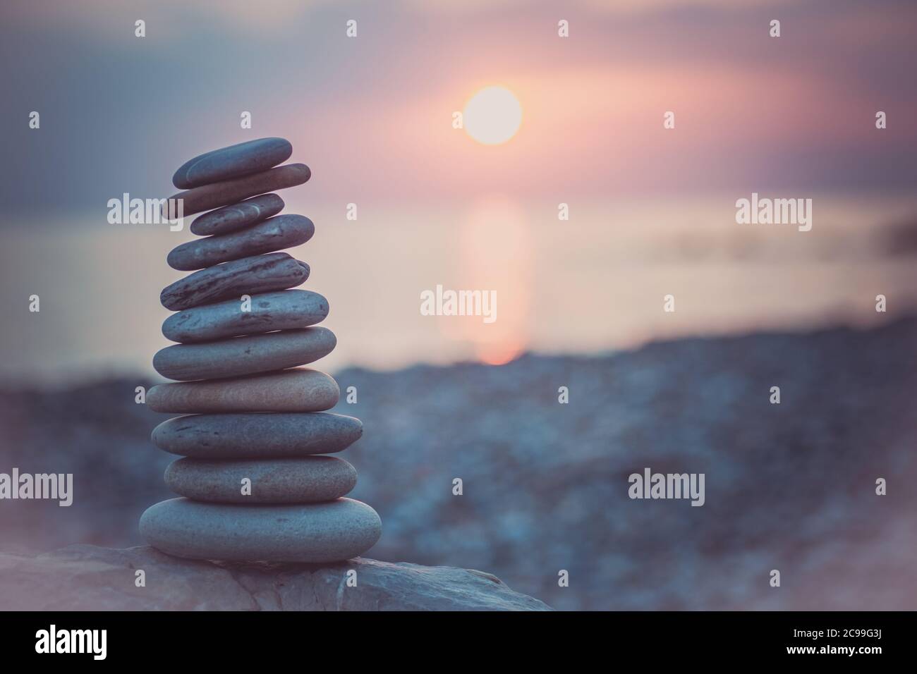 Pietre piramide sulla sabbia simboleggiando zen, armonia, equilibrio. Oceano al tramonto sullo sfondo. Foto Stock