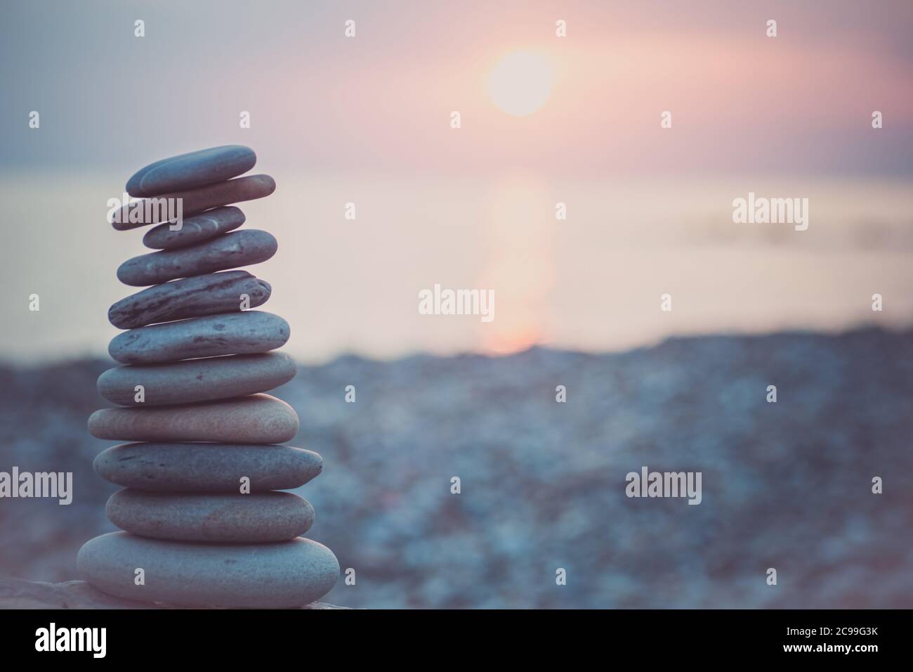 Pietre piramide sulla sabbia simboleggiando zen, armonia, equilibrio. Oceano al tramonto sullo sfondo. Foto Stock
