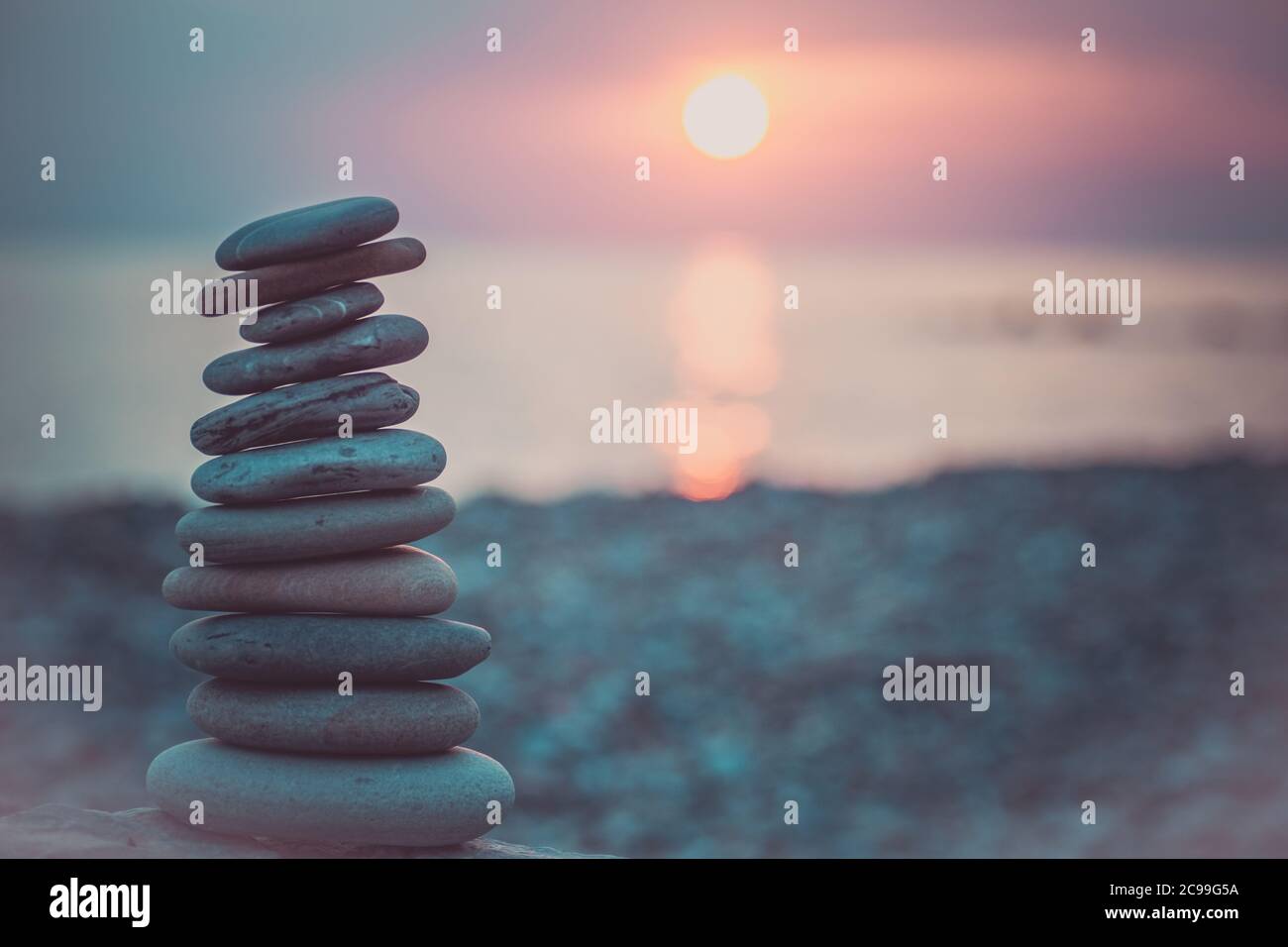 Pietre piramide sulla sabbia simboleggiando zen, armonia, equilibrio. Oceano al tramonto sullo sfondo. Foto Stock