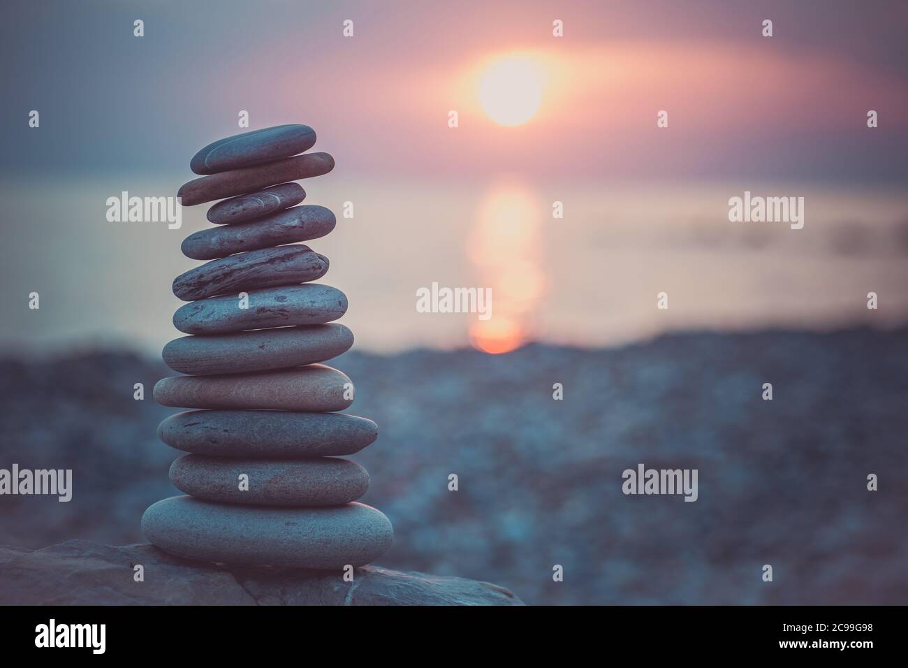 Pietre piramide sulla sabbia simboleggiando zen, armonia, equilibrio. Oceano al tramonto sullo sfondo. Foto Stock