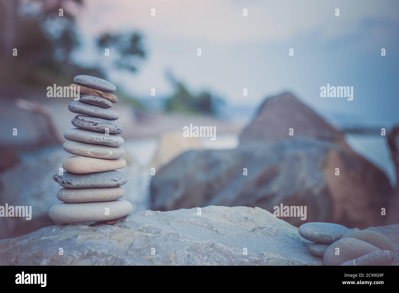 Pietre piramide sulla sabbia simboleggiando zen, armonia, equilibrio. Oceano al tramonto sullo sfondo. Foto Stock