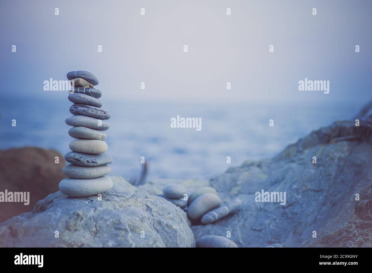 Pietre piramide sulla sabbia simboleggiando zen, armonia, equilibrio. Oceano al tramonto sullo sfondo. Foto Stock