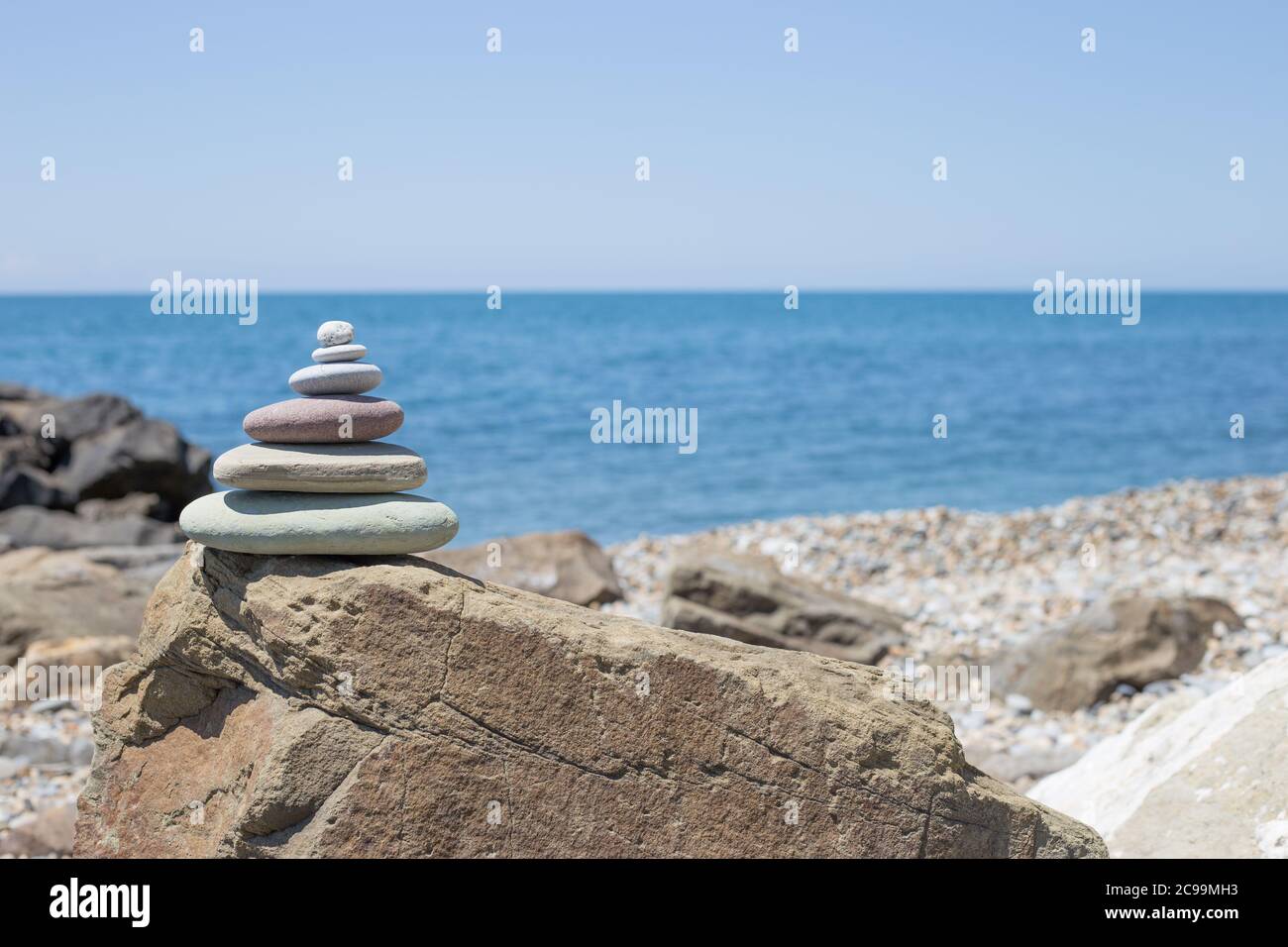 Piramide di pietre sulla sabbia che simboleggiano zen, armonia, equilibrio. Oceano al tramonto in background Foto Stock