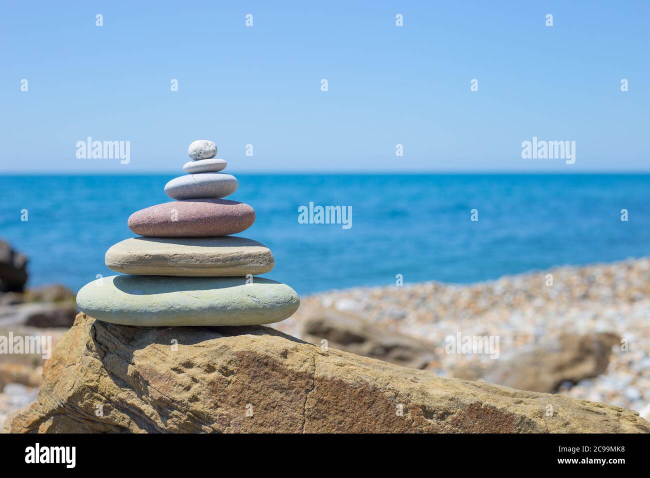 Piramide di pietre sulla sabbia che simboleggiano zen, armonia, equilibrio. Oceano al tramonto in background Foto Stock