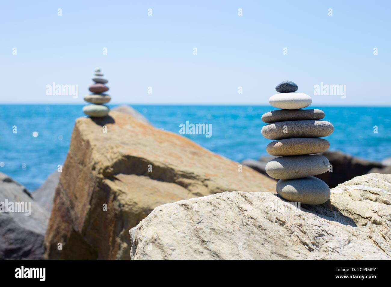 Piramide di pietre sulla sabbia che simboleggiano zen, armonia, equilibrio. Oceano al tramonto in background Foto Stock