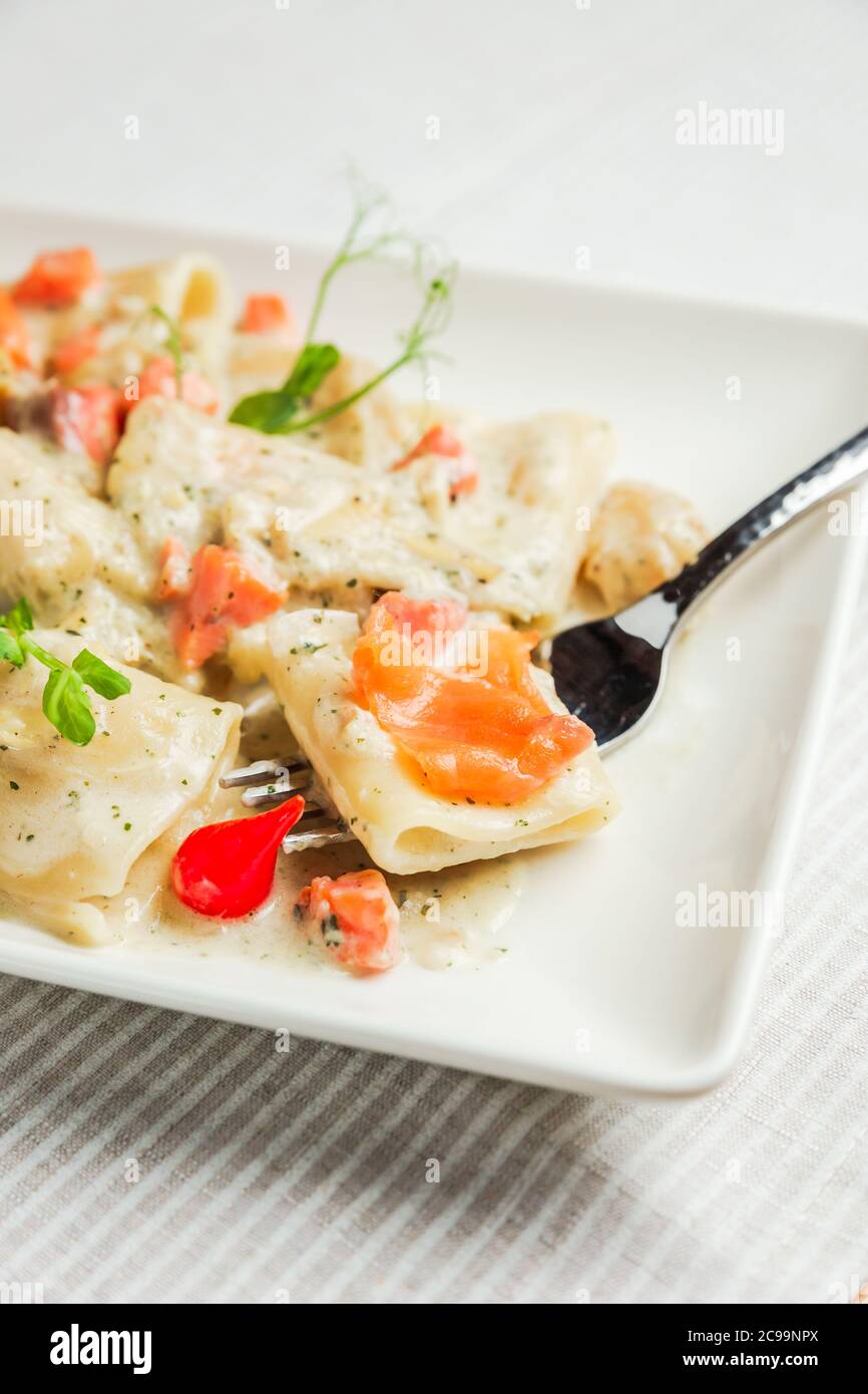 Un primo piano di pasta di paccheri con salsa di panna e salmone su una forchetta, su un piatto bianco Foto Stock