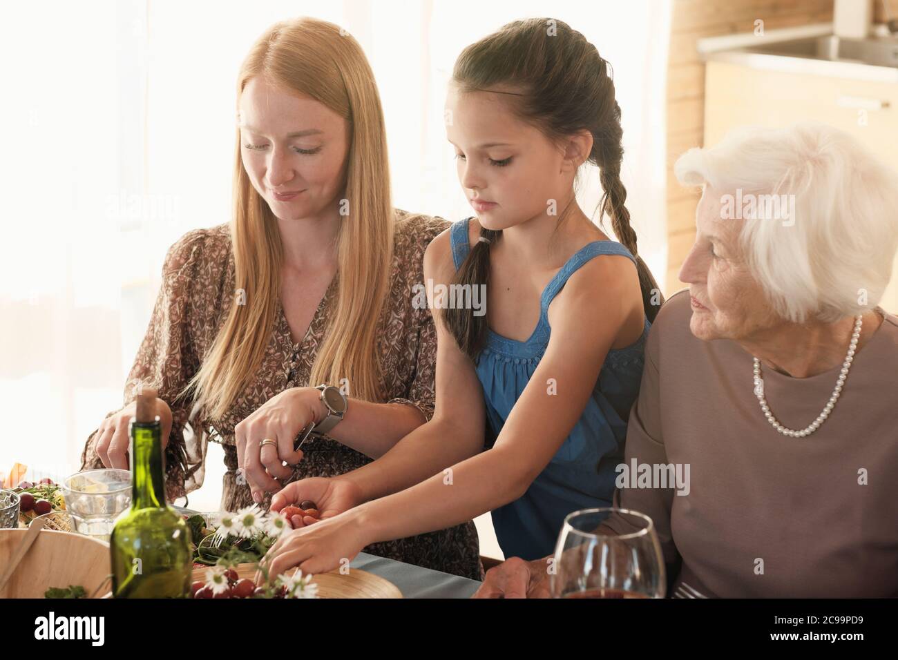 Famiglia di tre nonna madre e figlia seduta al tavolo e cena insieme Foto Stock
