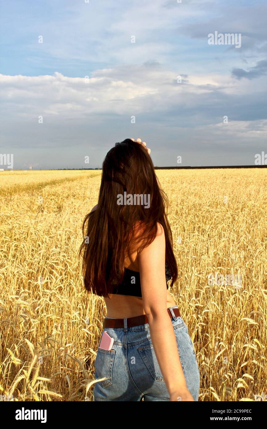 Giovane felice bella ragazza snella con capelli lunghi e un cappello in un campo di grano. Paesaggio estivo Foto Stock