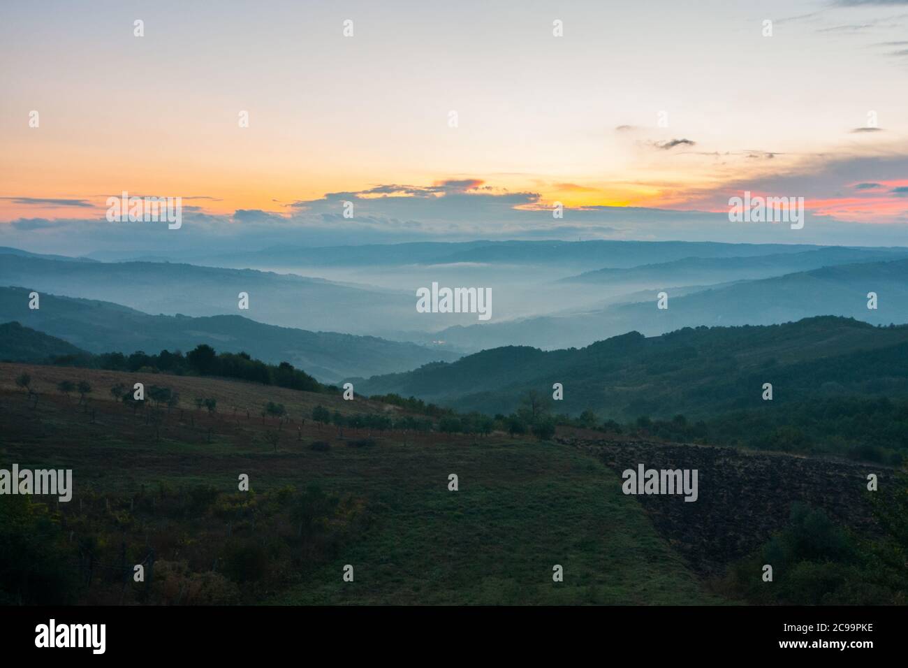 Tipico paesaggio collinare italiano all'alba, con verdi colline e un cielo blu, rosa e giallo Foto Stock