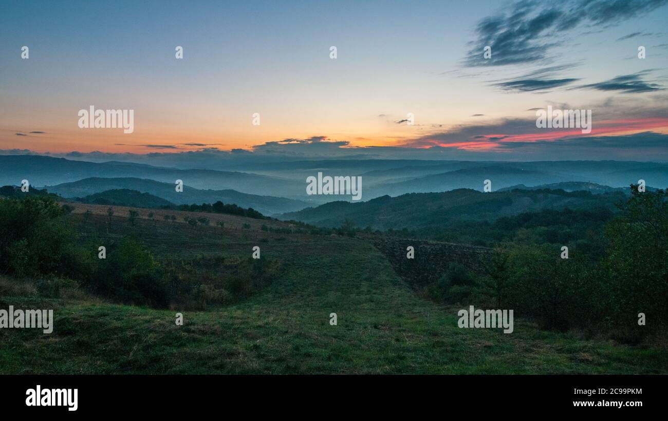 Tipico paesaggio collinare italiano all'alba, con verdi colline e un cielo blu, rosa e giallo Foto Stock
