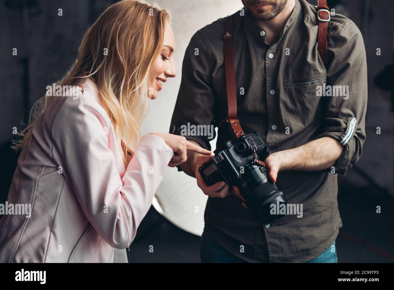 bella ragazza impressionante che punta alla foto mentre lavora con un fotografo, ragazza allegra che dà consigli per il fotografo in studio Foto Stock