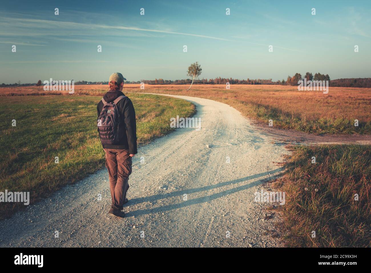 Un uomo con uno zaino va strada ghiaiata in un giorno d'autunno Foto Stock