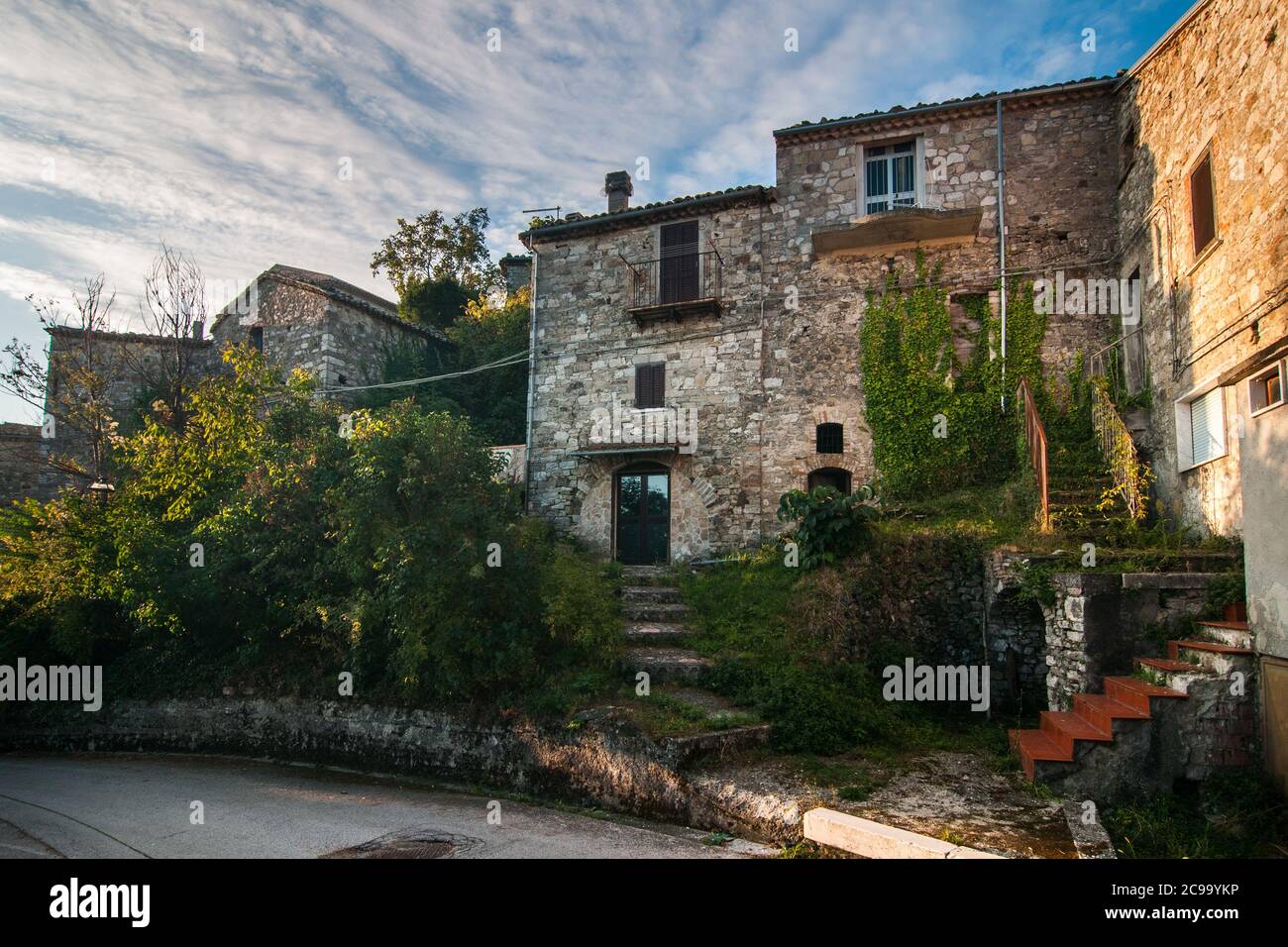 Particolare di uno degli edifici in mattoni e alcuni verdi alberi in una strada tipica del villaggio antico di Torella del Sannio in Molise Foto Stock