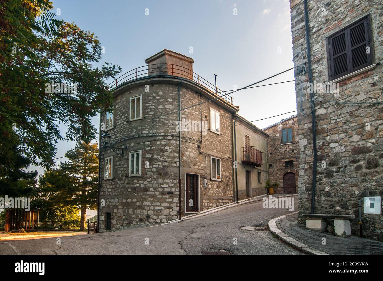 Particolare di alcuni edifici in mattoni, di alcune case antiche e di alcuni alberi verdi in una strada tipica dell'antico borgo di Torella del Sannio in Molise Foto Stock
