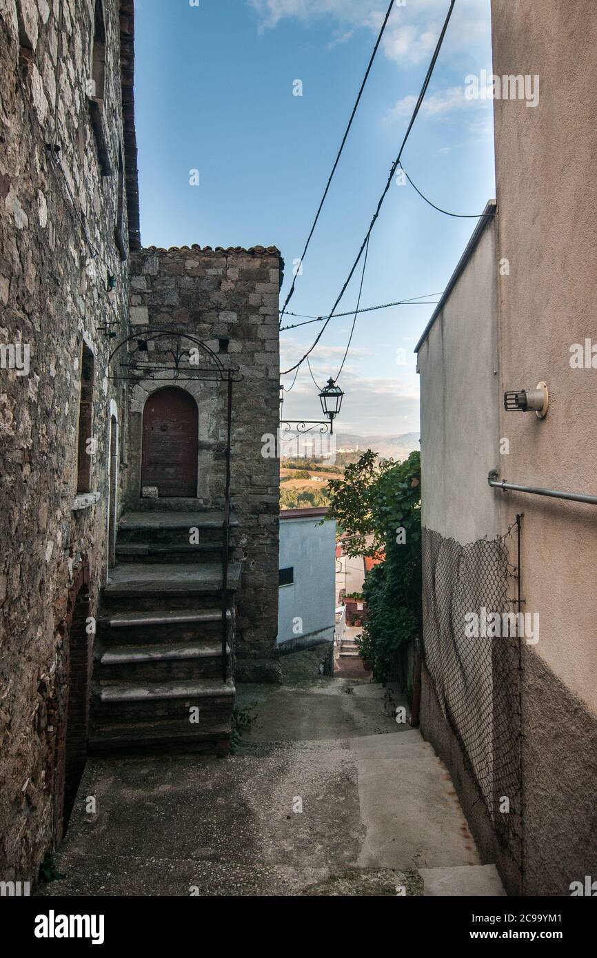 Particolare di alcuni edifici in mattoni, di alcune case antiche, di una lanterna e di alcuni alberi verdi in una strada tipica dell'antico borgo di Torella del Sannio i. Foto Stock