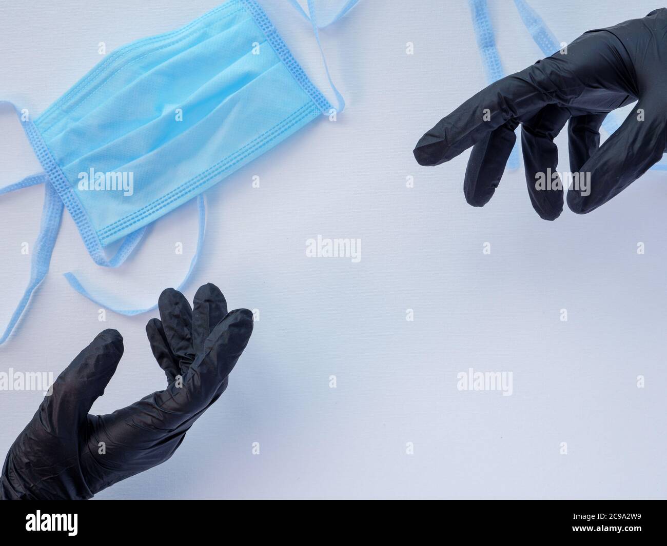 Due mani in guanti di lattice neri che si allungano l'una verso l'altra. Maschera medica protettiva blu su sfondo bianco. Protezione antivirale. Foto Stock