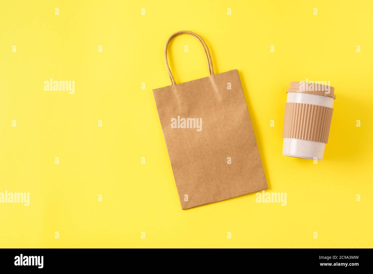 Mockup di borsa per la spesa in carta kraft con manici sulla superficie gialla, tazza da caffè portatile riutilizzabile per i viaggi. Tazza di prelievo con tappo antigoccia. Foto Stock
