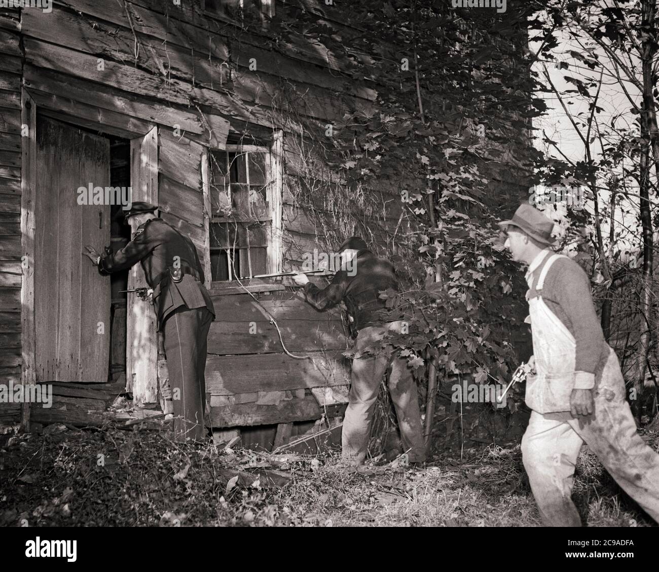 1940S POLIZIOTTO E POSSE ARMATI DI ARMI IN AVVICINAMENTO ABBANDONATO SHACK ALLA RICERCA DI SCAPPATELLE NASCONDENDOSI DENTRO - P244 HAR001 HARS MASCHI ORDINE DI RISCHIO UFFICIALE B&W TRISTEZZA FORZE DELL'ORDINE COP RICERCA GRANDANGOLO ARMATO PROTEGGERE AVVENTURA PERICOLOSA SCOPERTA PROTEZIONE FORZA STRATEGIA CORAGGIO E ECCITAZIONE LEADERSHIP ABBANDONATA AUTORITÀ OCCUPAZIONI SHACK UNIFORMI CRIMINALI FUGGIRE MOTION BLUR FUGA CONCETTUALE RICERCA UNIFORMED CROOKS UFFICIALI POLIZIOTTI POSSE CAUTO COOPERAZIONE POLIZIOTTI FUGGITIVI COINVOLGENDO METÀ ADULTI MID-ADULT UOMO HA VOLUTO DIFFIDARE AVVICINARSI BADGE NERO E BIANCO Foto Stock