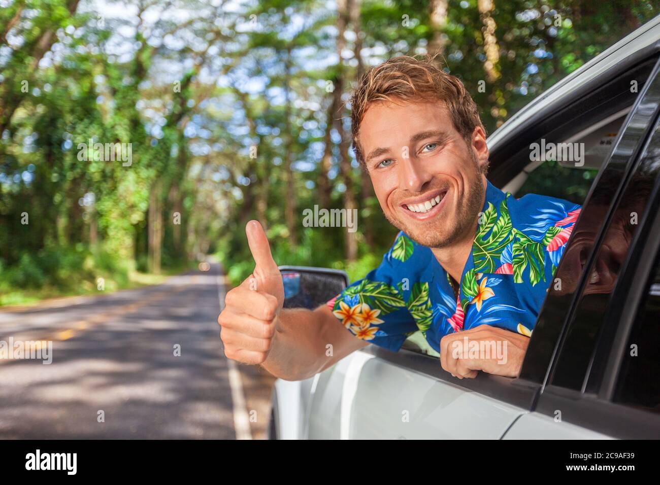 Buon conducente di auto uomo guida sicuro su strada viaggio facendo pollici in su soddisfazione di auto a noleggio. Sorridente giovane modello maschile Foto Stock