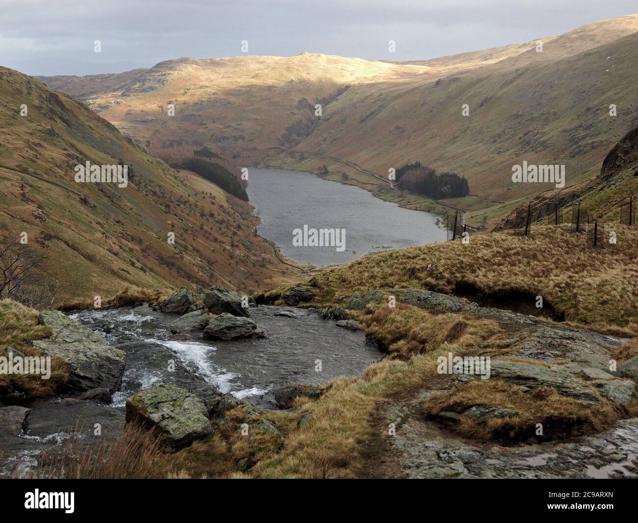 Vista da Mardale Beck un tumbling upland ruscello sotto High Street sopra la ruvida Haweswater e lontano Sunlit Lake District Fells Cumbria, Inghilterra, Regno Unito Foto Stock