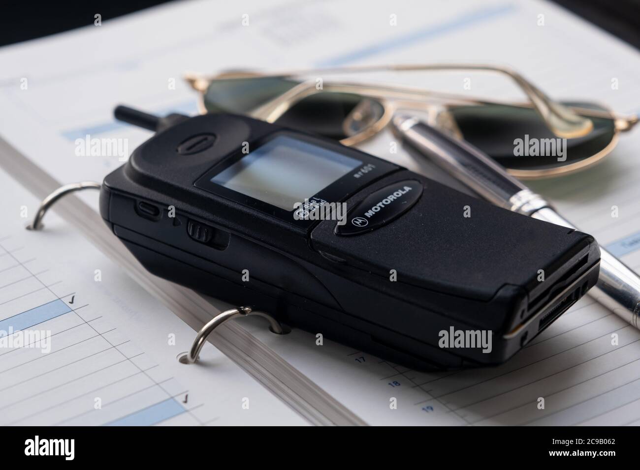 Telefono cellulare degli anni novanta, una penna fontana d'argento e un paio di occhiali da sole seduti sopra un diario di grande formato. Foto Stock