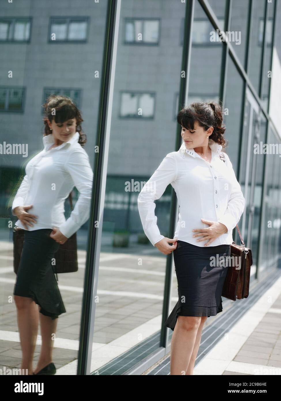 Donna matura perdere peso e guardando Mirror in Office Window Foto Stock