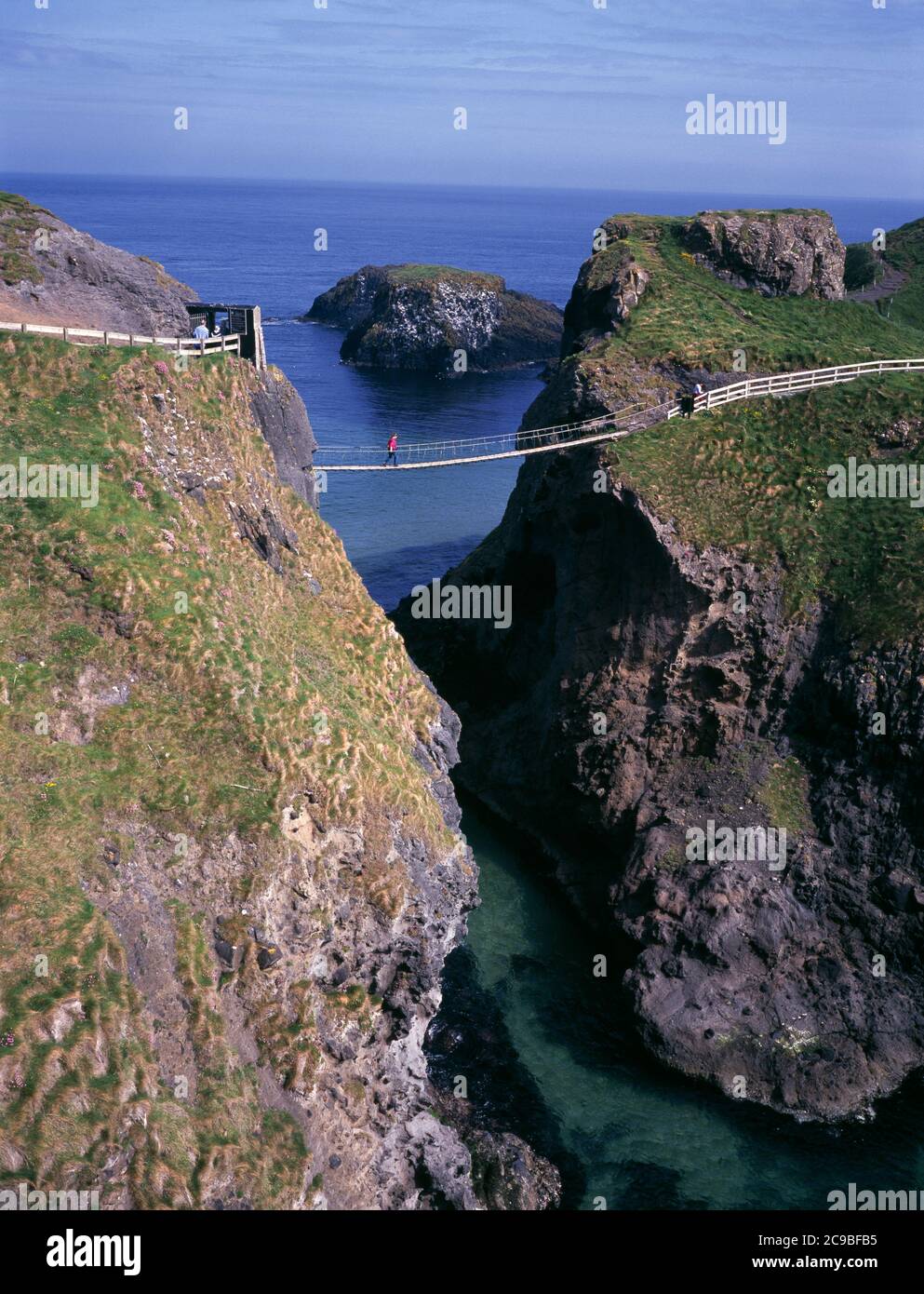 Ponte di corda Carrick-A-Rede con escursionisti che attraversano, vicino a Ballintoy, Contea di Antrim, Irlanda del Nord, Regno Unito Foto Stock