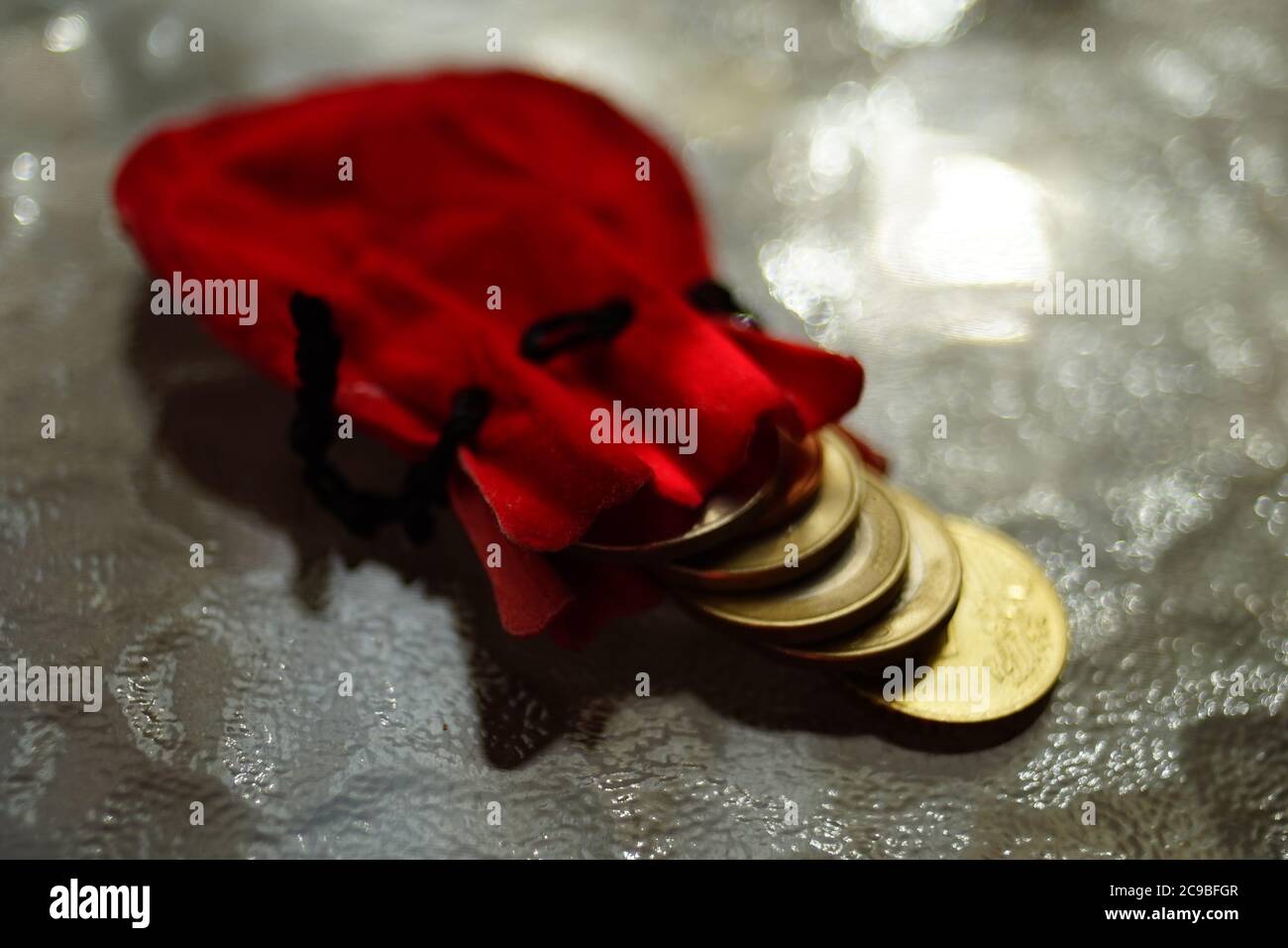 Monete d'oro in un sacchetto rosso su un tavolo di vetro Foto Stock