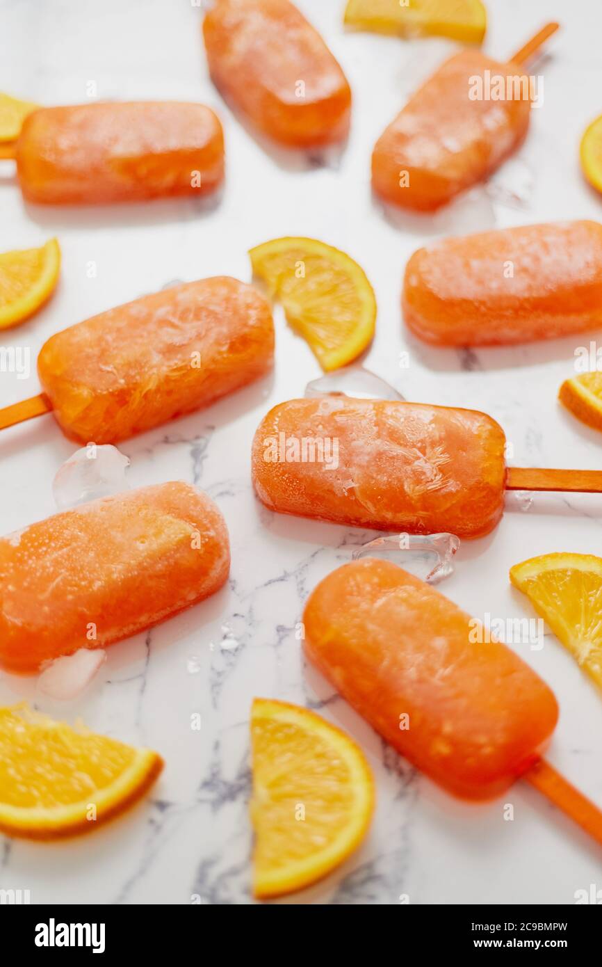 Pop sicle surgelate fatte in casa con arance fresche oragniche poste con cubetti di ghiaccio sul tavolo di marmo Foto Stock